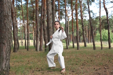 Photo of Cute little girl in kimono practicing karate in forest