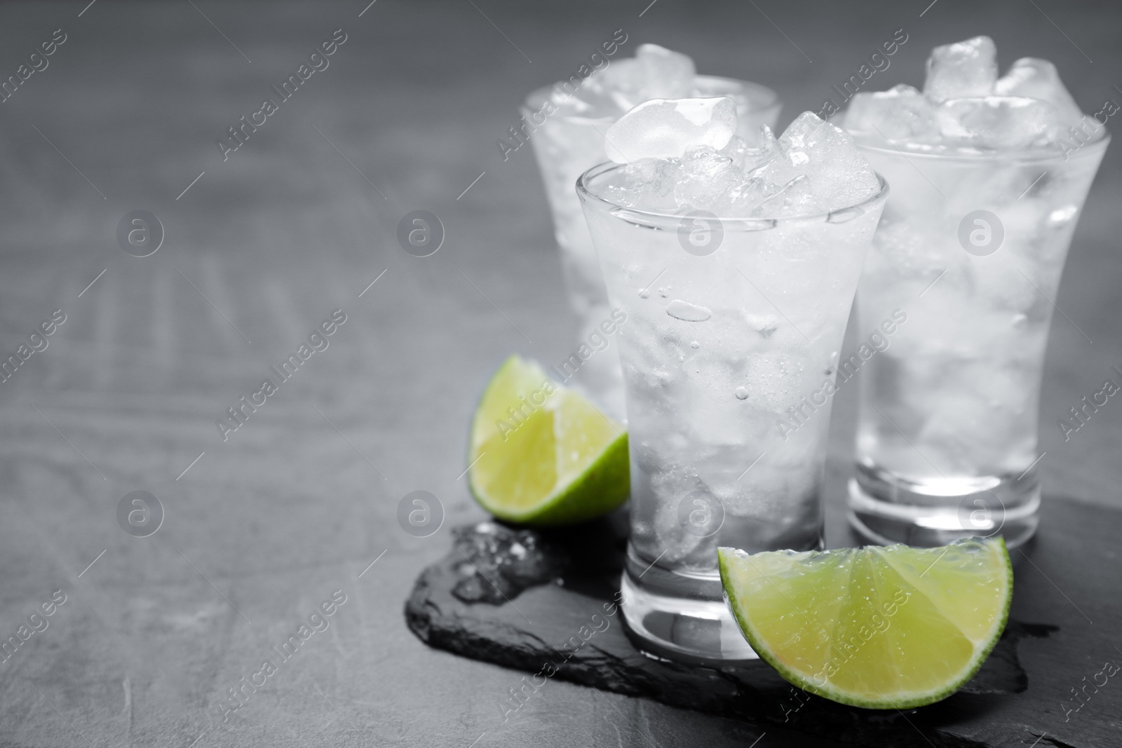 Photo of Shot glasses with vodka, ice and lime on grey table. Space for text