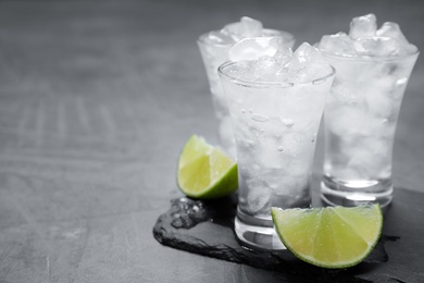 Shot glasses with vodka, ice and lime on grey table. Space for text