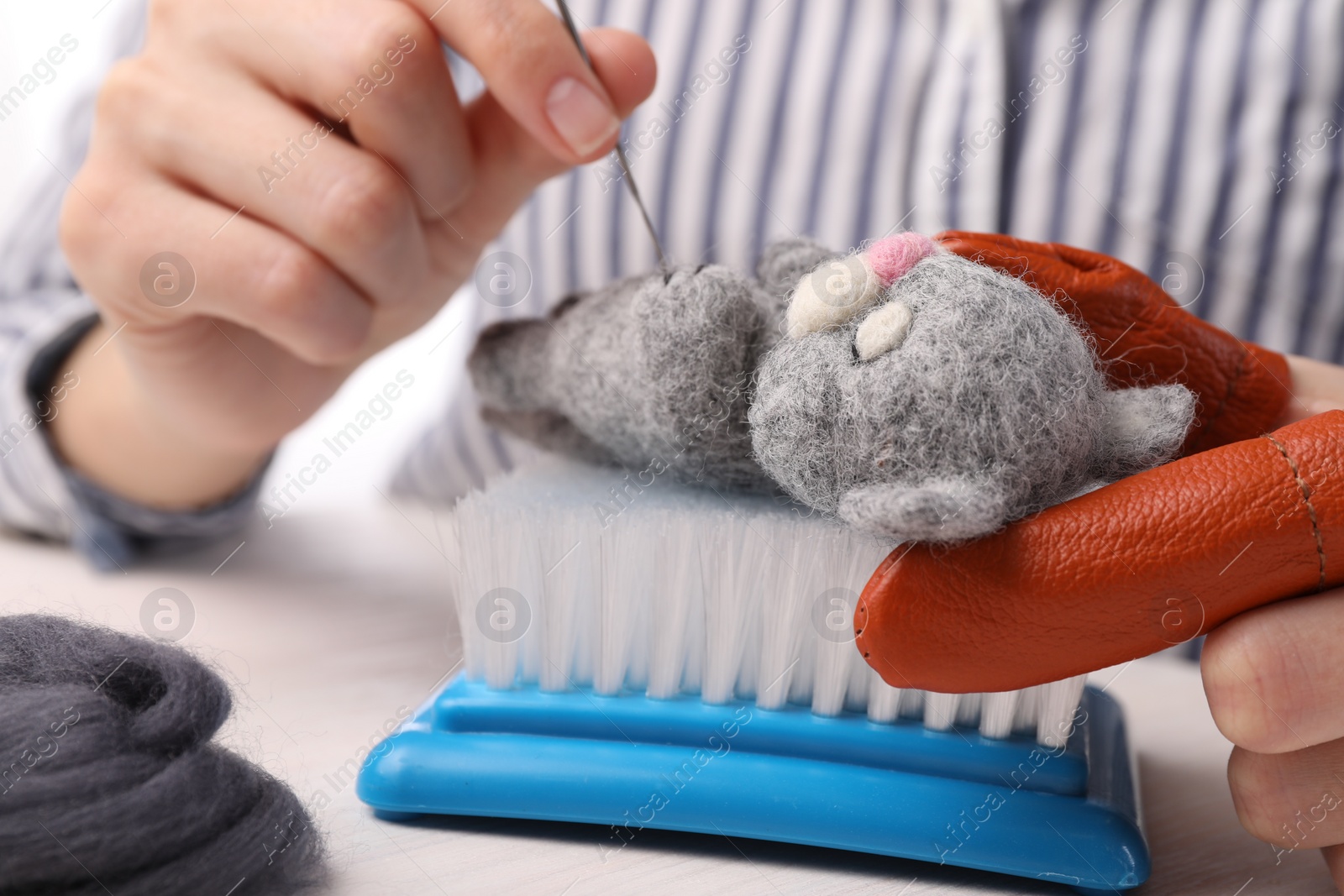 Photo of Woman felting toy cat from wool at light table, closeup