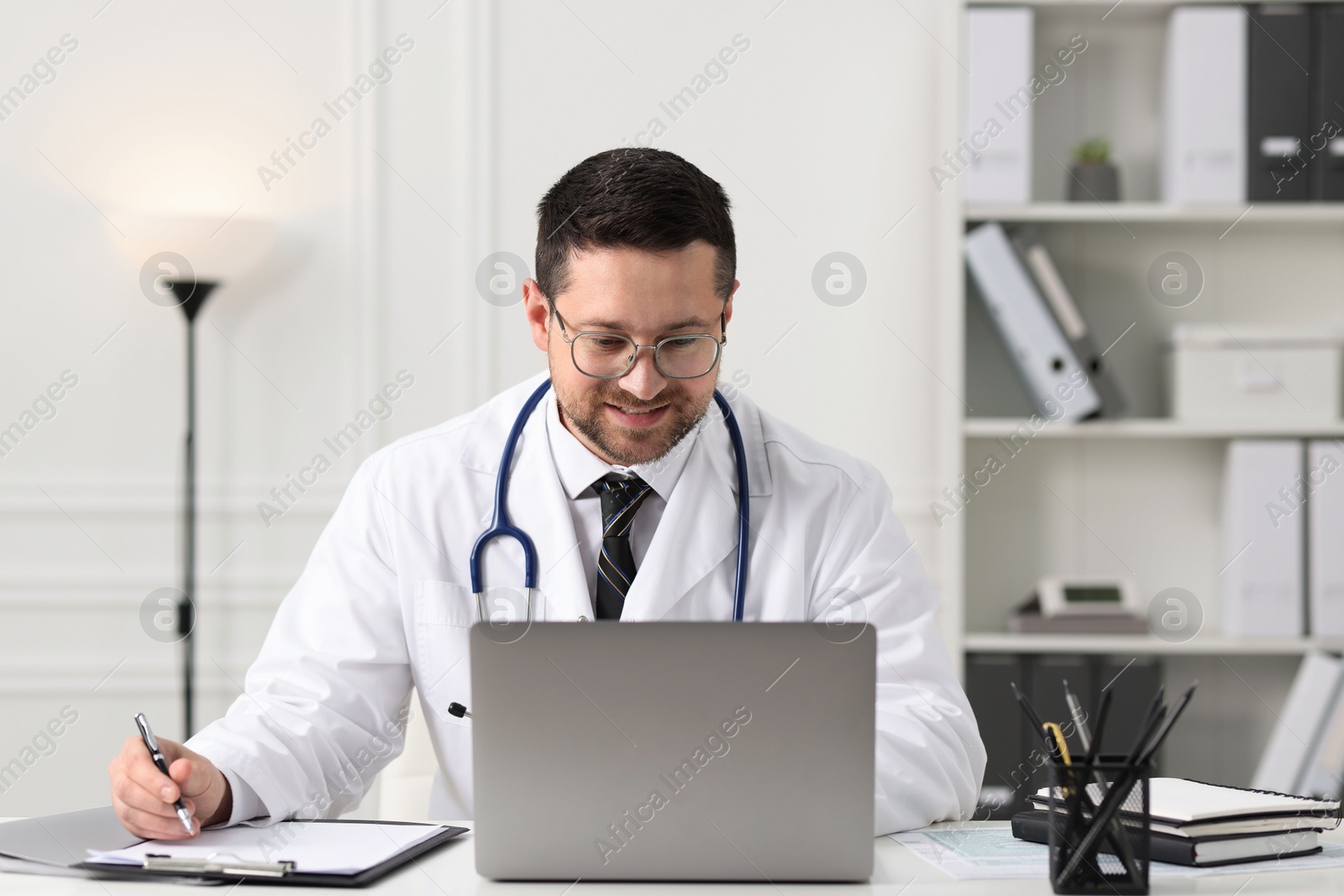 Photo of Doctor having online consultation via laptop at table in clinic