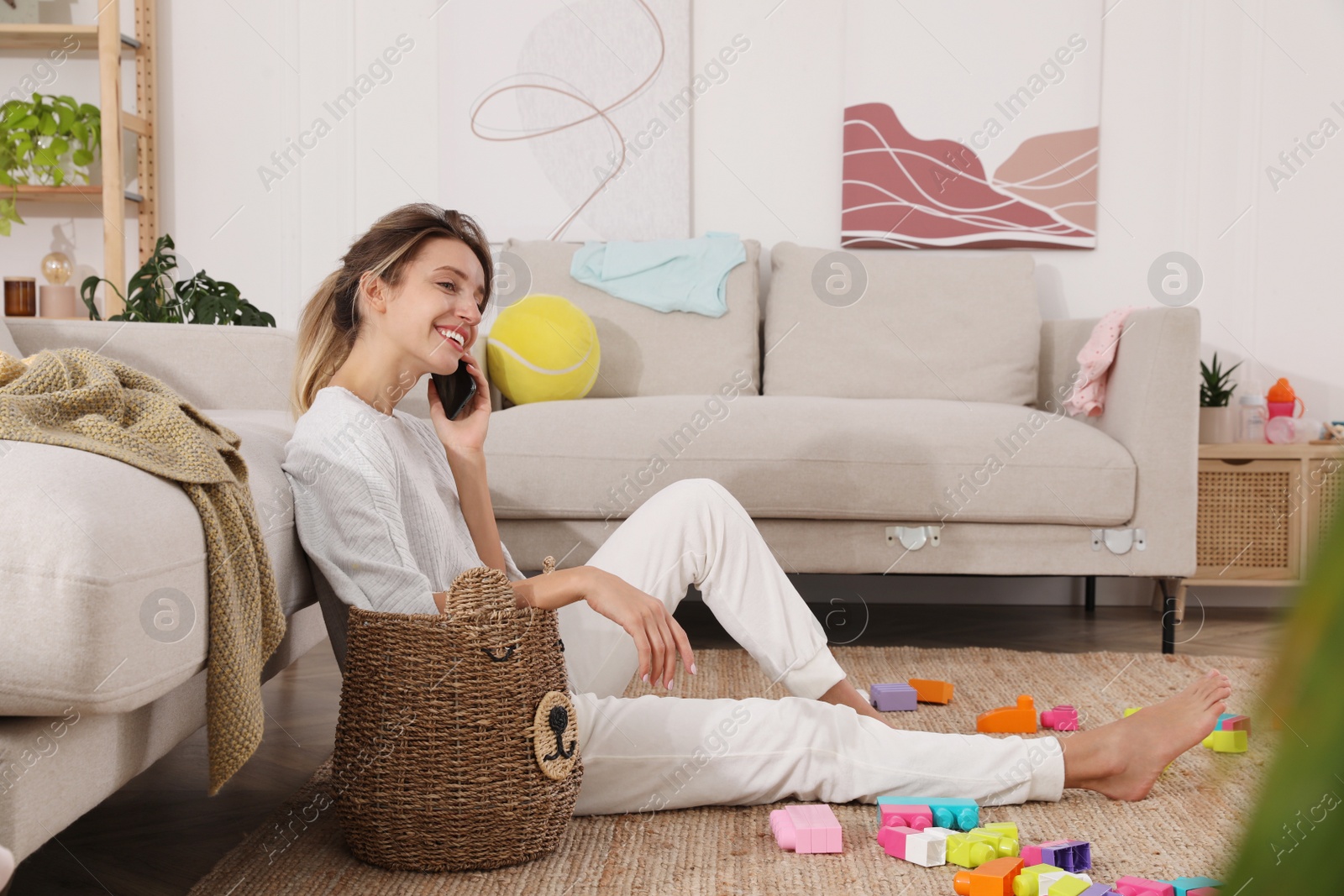 Photo of Young mother talking on phone in messy living room