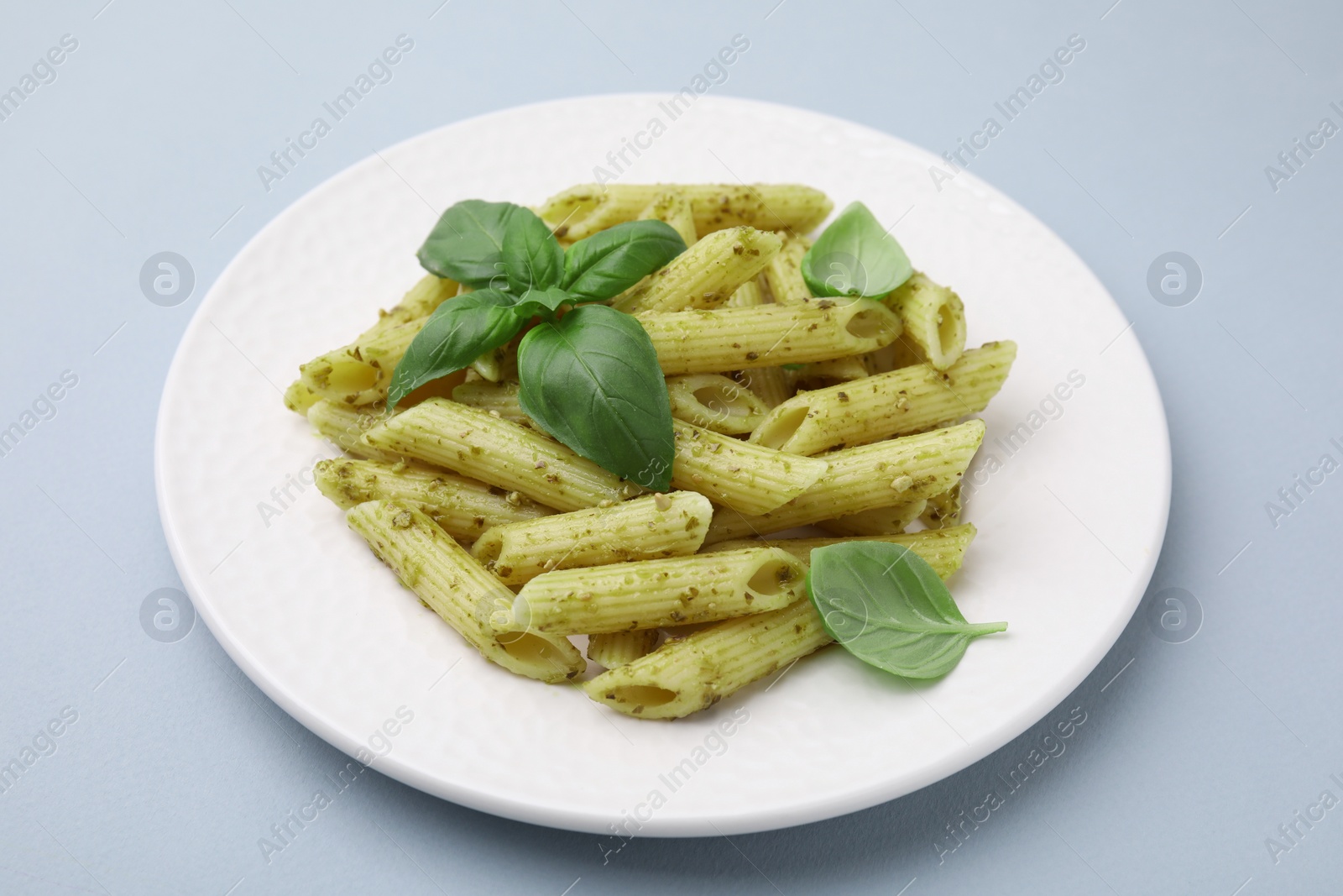 Photo of Delicious pasta with pesto sauce and basil on light grey background, closeup