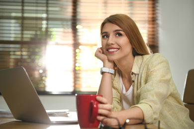 Photo of Young woman with cup of drink relaxing at workplace
