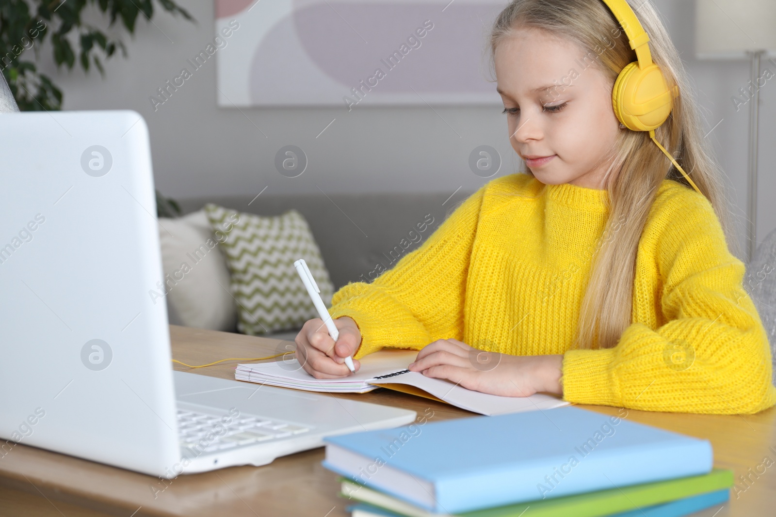 Photo of Cute little girl with modern laptop studying online at home. E-learning