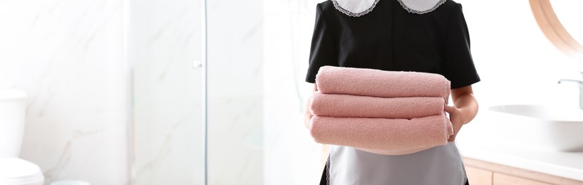 Image of Young chambermaid holding stack of fresh towels in bathroom, closeup view with space for text. Banner design