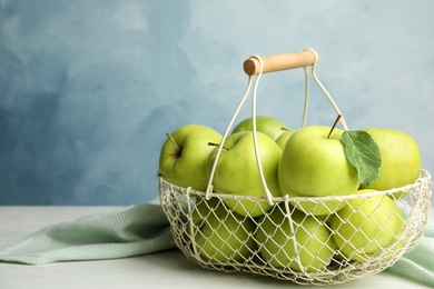 Metal basket of fresh ripe green apples on white wooden table against blue background, space for text