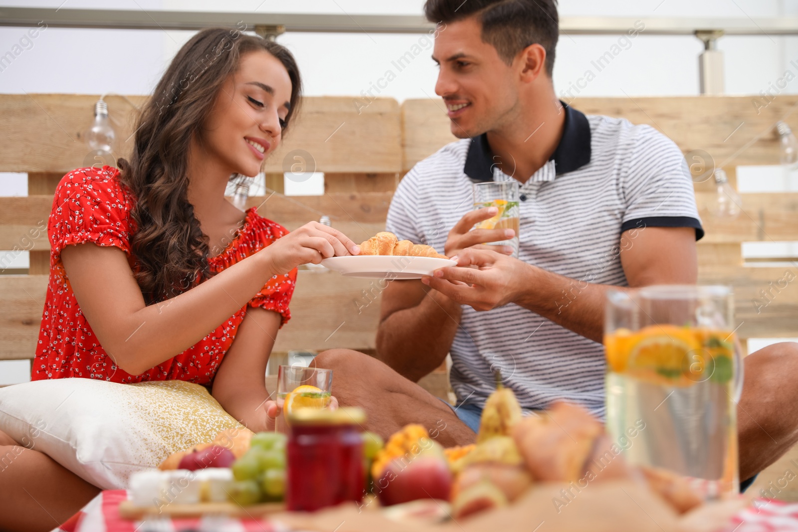 Photo of Happy couple with tasty food and drinks imitating picnic at home