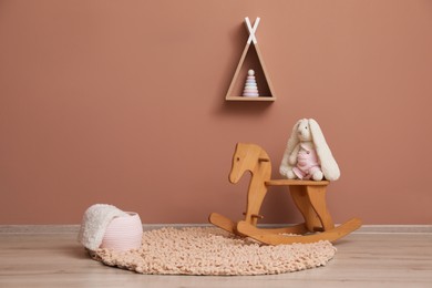Photo of Rocking horse with bunny toy, wicker basket and wigwam shaped shelf on pink wall