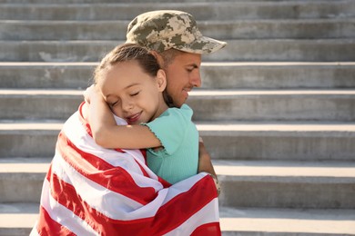 Soldier with flag of USA and his little daughter hugging outdoors, space for text