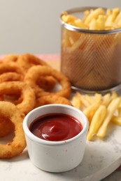 Photo of Tasty ketchup, fries and onion rings on board, selective focus