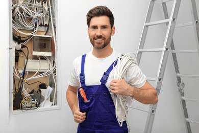 Photo of Smiling electrician with wires near open fuse box indoors