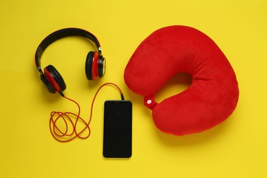 Photo of Red travel pillow, smartphone and headphones on yellow background, flat lay