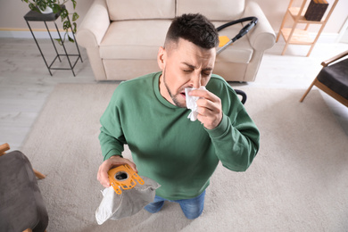 Photo of Man with vacuum cleaner bag suffering from dust allergy at home, above view