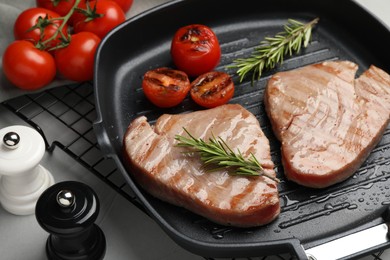 Photo of Delicious tuna steaks with rosemary and tomatoes on grey table, closeup