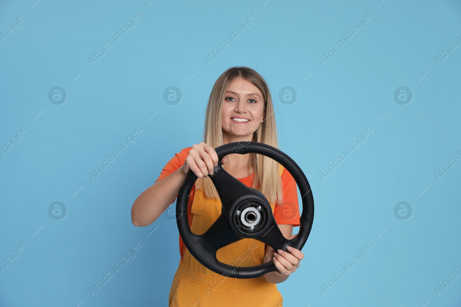Photo of Happy young woman with steering wheel on light blue background