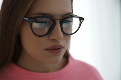 Young woman wearing glasses on blurred background, closeup. Ophthalmology service