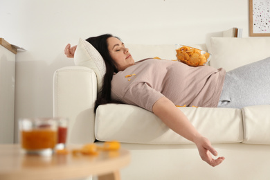 Photo of Lazy overweight woman with chips resting on sofa at home