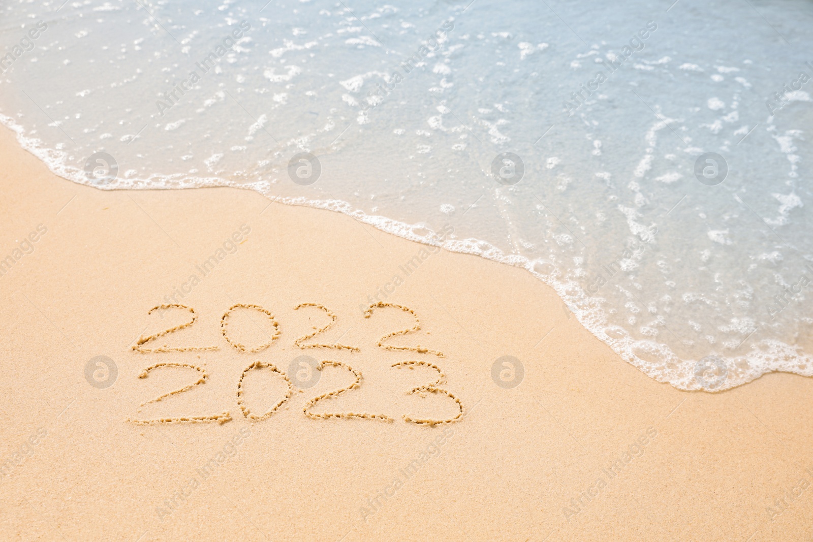 Photo of Dates written on sandy beach. 2022 washed by sea wave as New 2023 Year coming