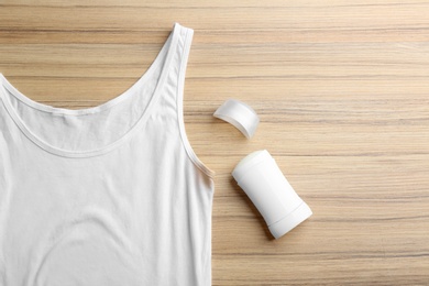 White undershirt with stain and deodorant on wooden background, top view
