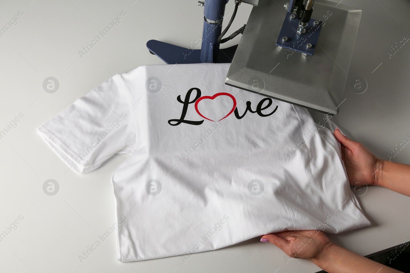 Photo of Printing logo. Woman with t-shirt using heat press at white table, above view