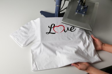 Photo of Printing logo. Woman with t-shirt using heat press at white table, above view