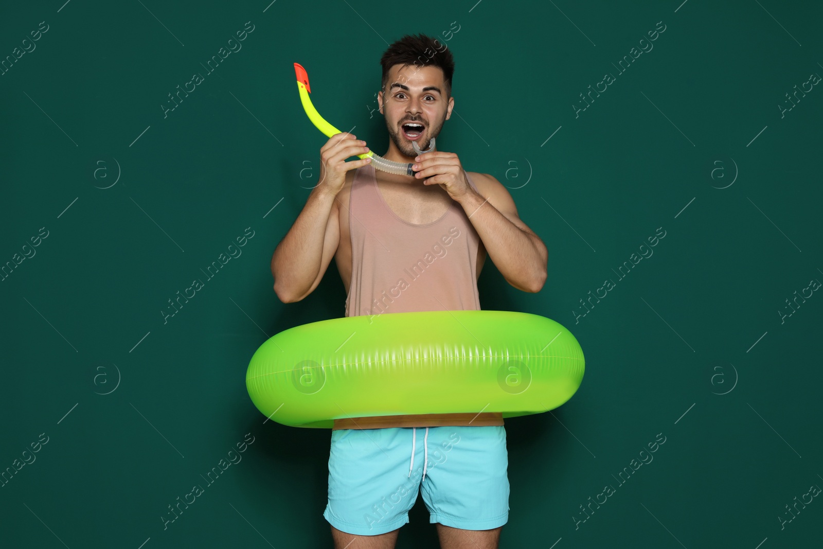 Photo of Funny young man with bright inflatable ring on dark green background