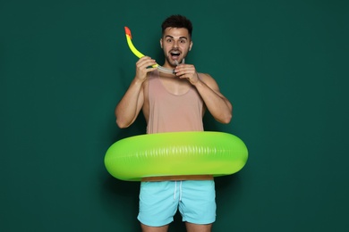 Photo of Funny young man with bright inflatable ring on dark green background