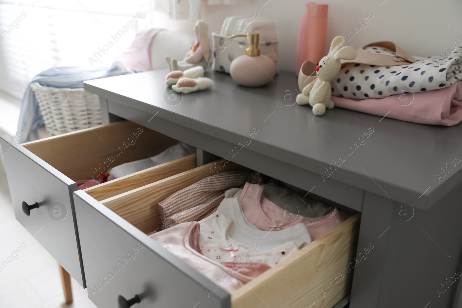 Photo of Open cabinet drawers with baby clothes in child room