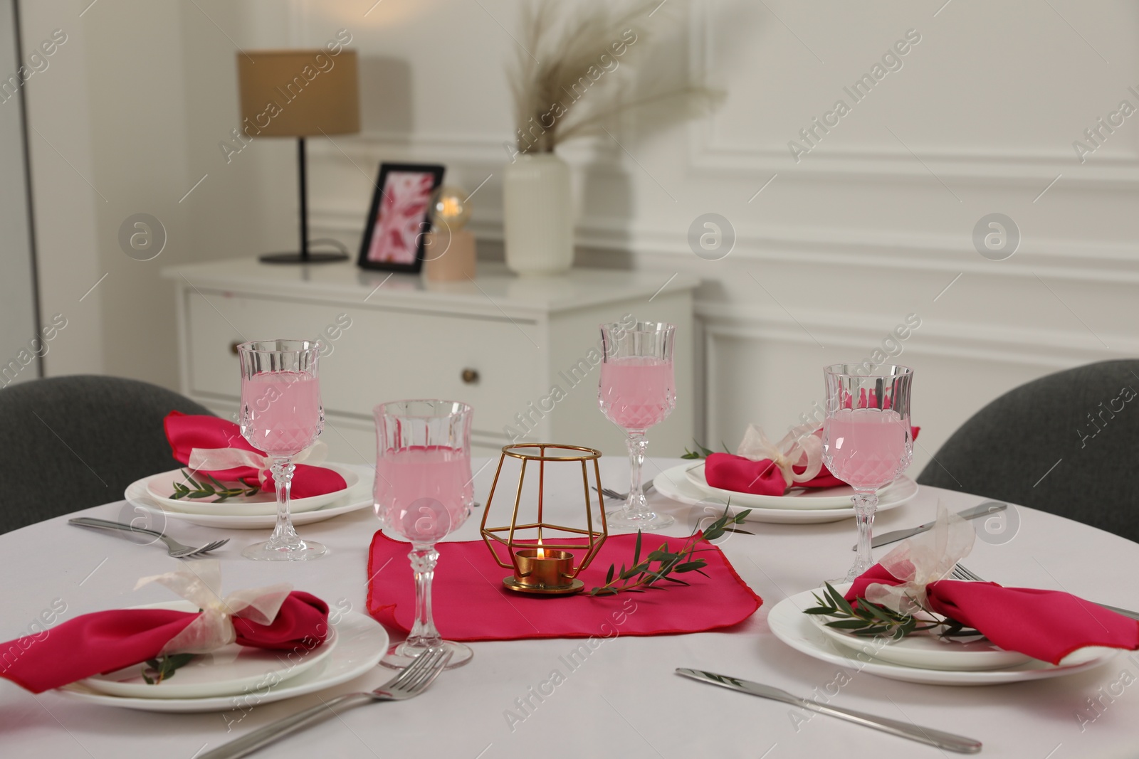 Photo of Color accent table setting. Glasses, plates, cutlery and pink napkins on table indoors