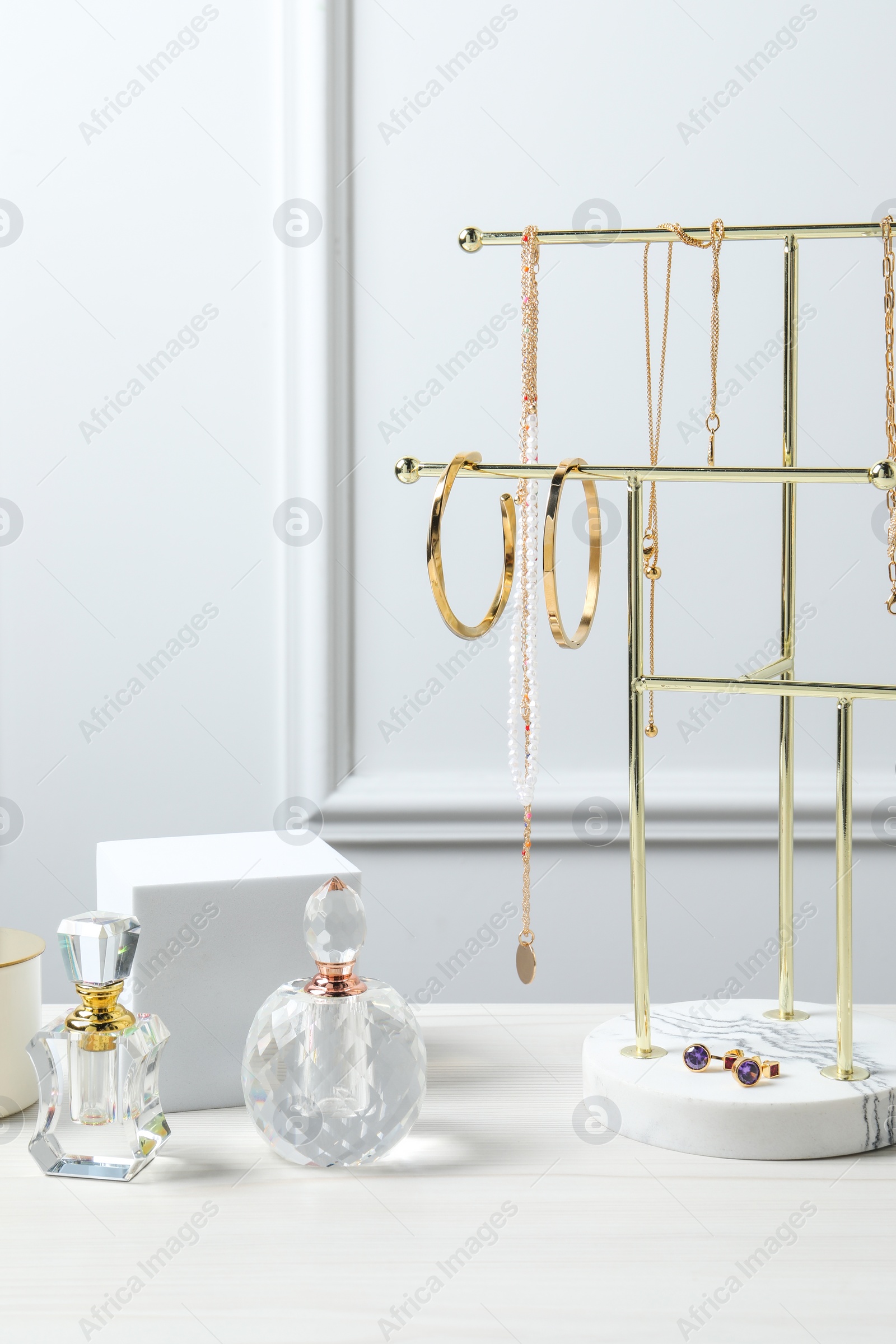 Photo of Holder with set of beautiful bijouterie and perfume bottles on white wooden table