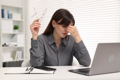 Overwhelmed woman sitting at table with laptop in office