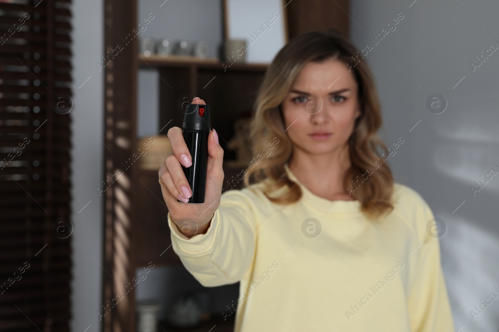 Photo of Young woman using pepper spray indoors, focus on hand