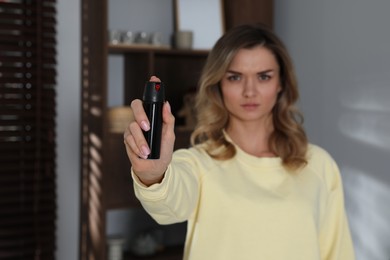 Photo of Young woman using pepper spray indoors, focus on hand