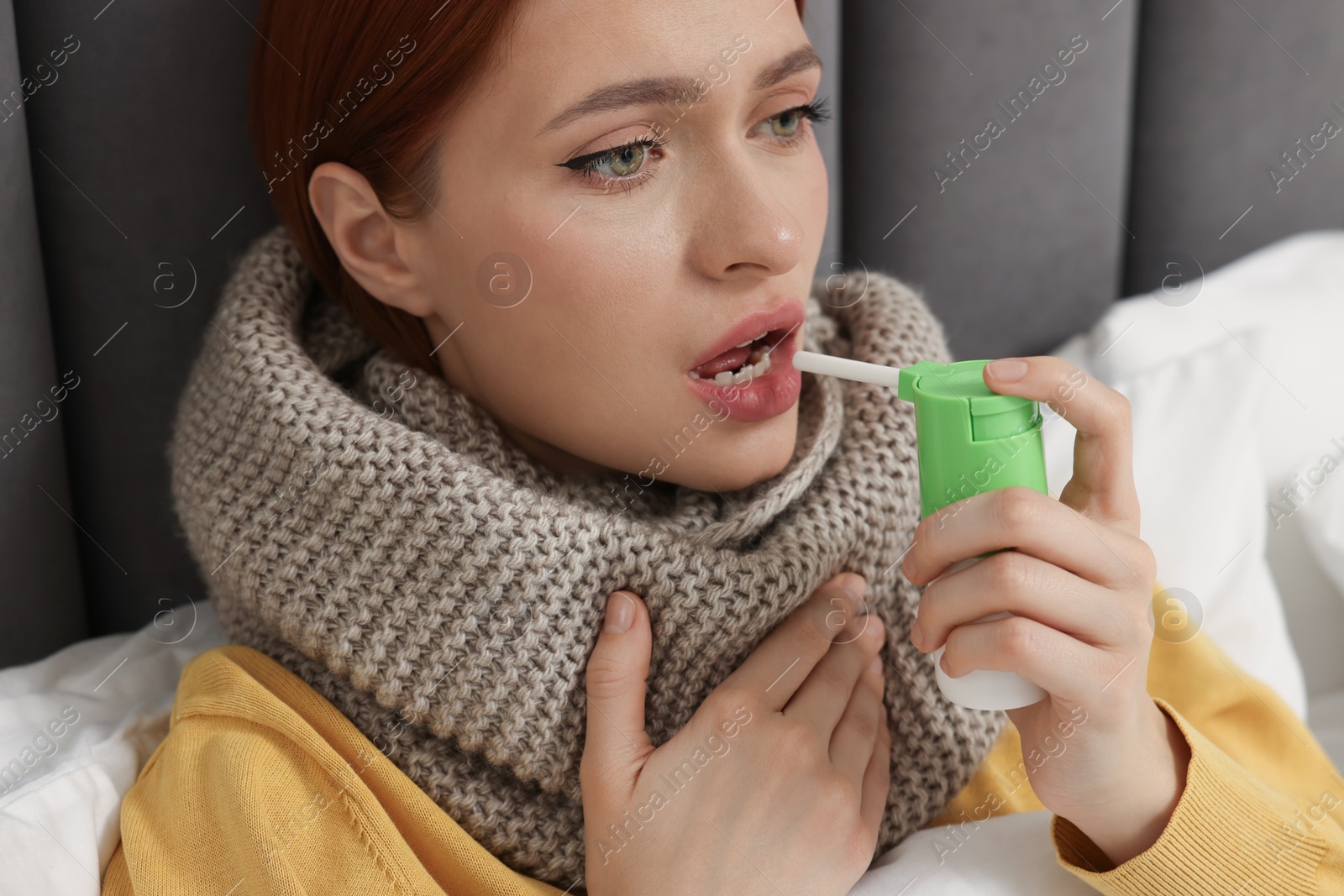 Photo of Young woman with scarf using throat spray in bed