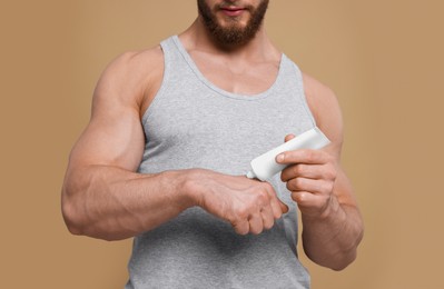 Man applying body cream onto his hand on pale brown background, closeup