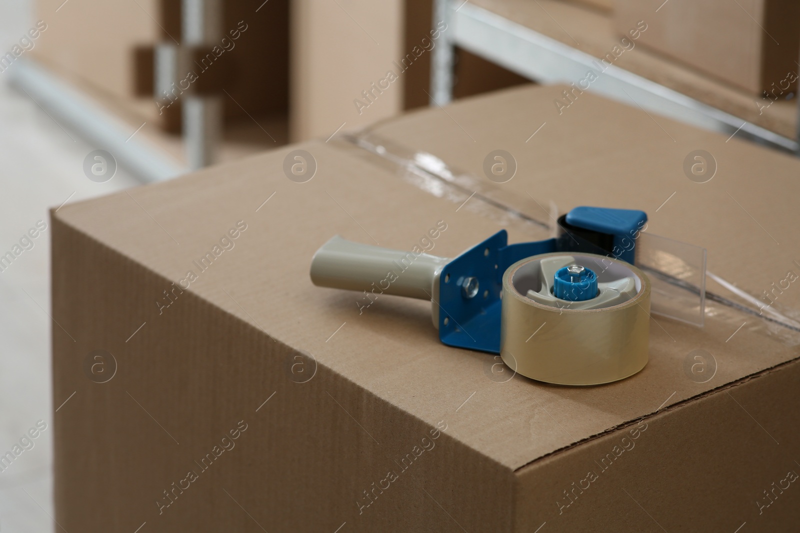 Photo of Adhesive tape dispenser on cardboard box indoors