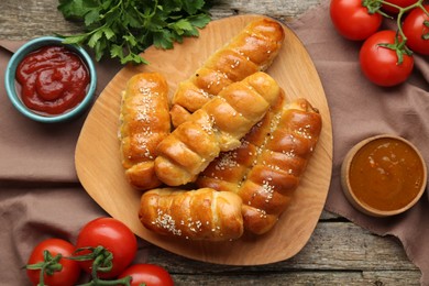 Photo of Delicious sausage rolls and ingredients on wooden table, flat lay