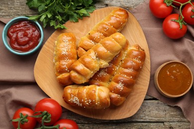 Delicious sausage rolls and ingredients on wooden table, flat lay