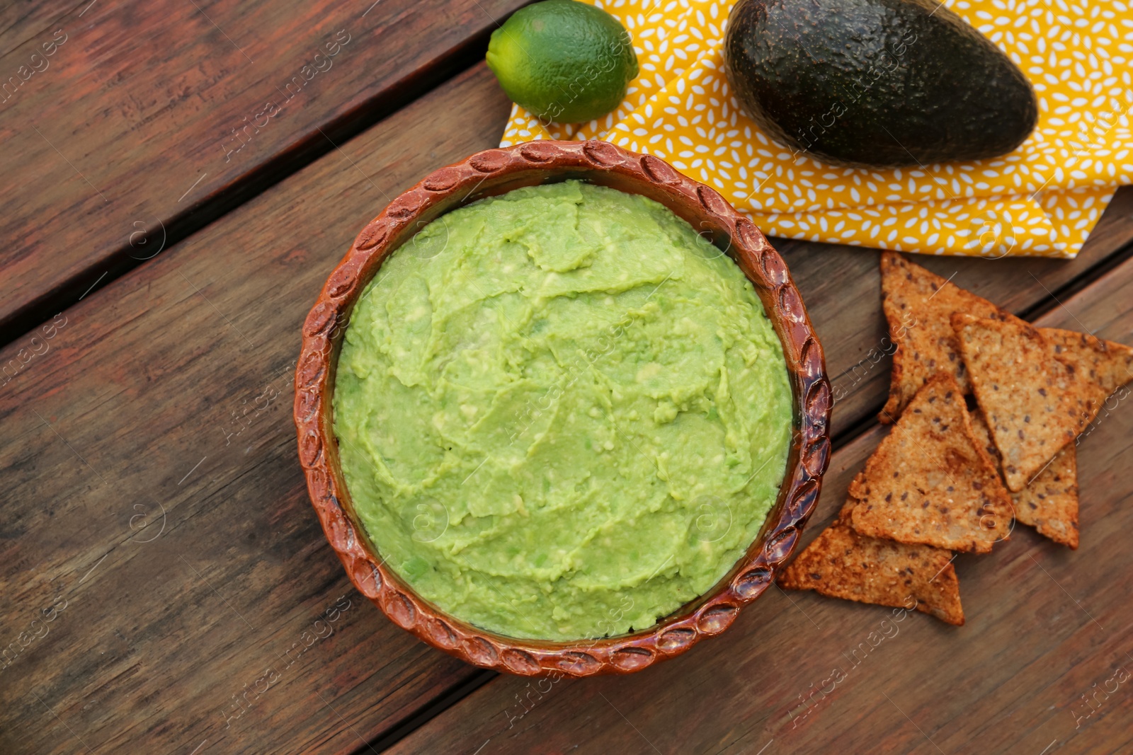 Photo of Delicious guacamole, avocados and nachos on wooden table, flat lay