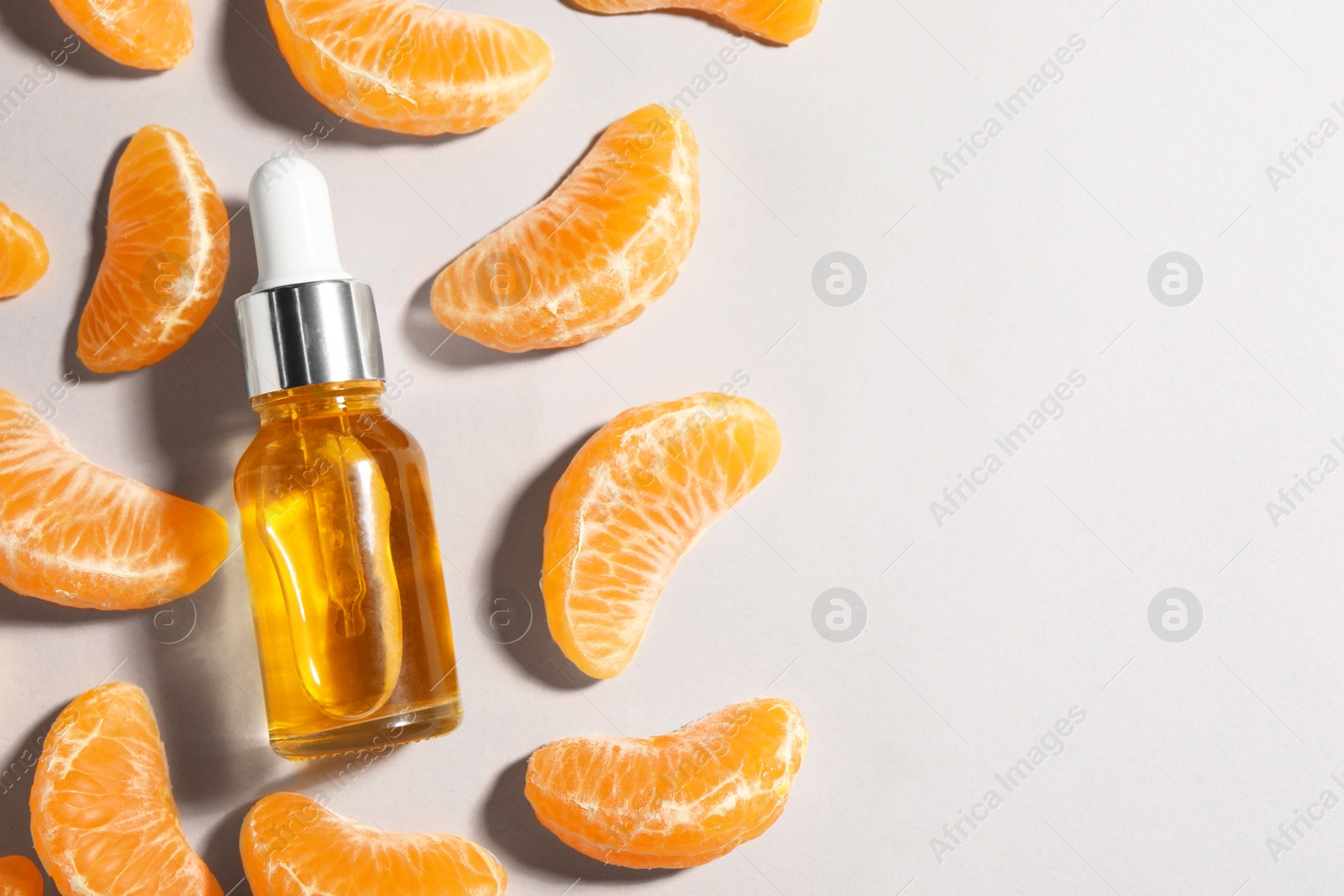 Photo of Aromatic tangerine essential oil in bottle and citrus fruit on grey table, flat lay. Space for text