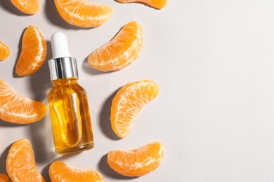 Photo of Aromatic tangerine essential oil in bottle and citrus fruit on grey table, flat lay. Space for text