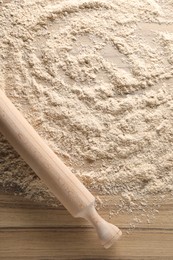 Photo of Scattered flour and rolling pin on wooden table, top view