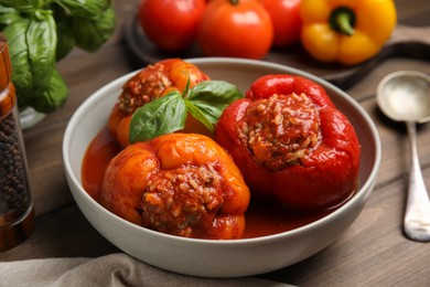 Photo of Delicious stuffed peppers with basil in bowl on wooden table