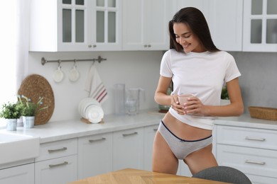 Young woman with cup wearing white t-shirt and comfortable underwear indoors. Space for text