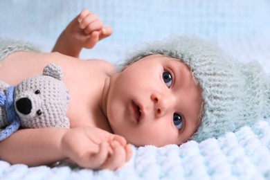 Photo of Cute newborn baby with crochet toy on light blue blanket, closeup