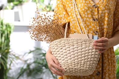 Photo of Woman holding beach bag with books and beautiful bouquet of dried flowers indoors, closeup