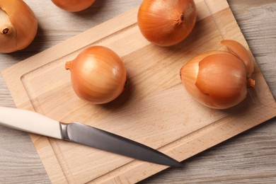 Photo of Many ripe onions and knife on wooden table, flat lay