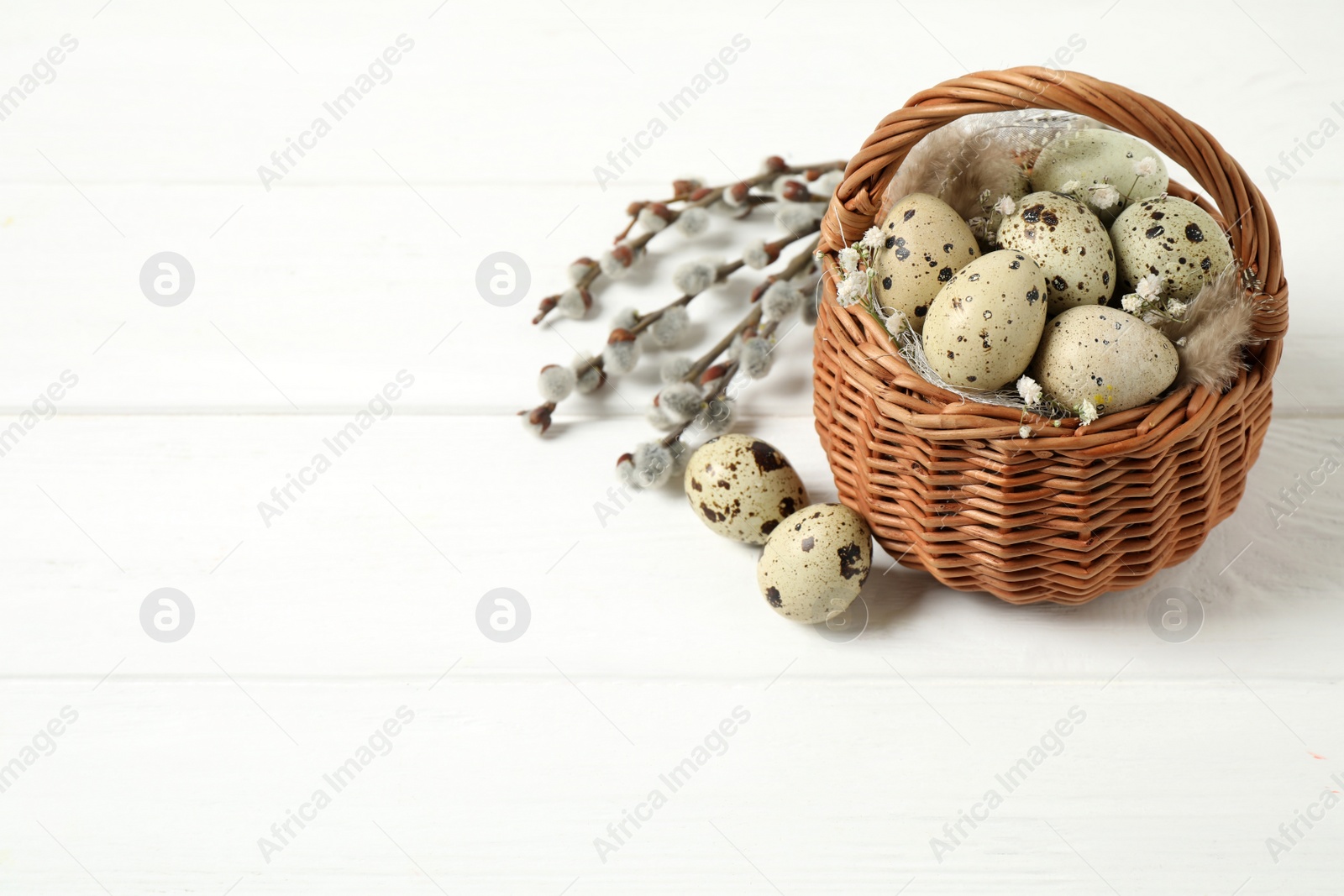 Photo of Quail eggs and flowers in wicker basket on white wooden background, space for text. Easter celebration