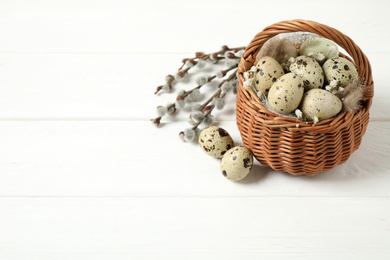 Quail eggs and flowers in wicker basket on white wooden background, space for text. Easter celebration